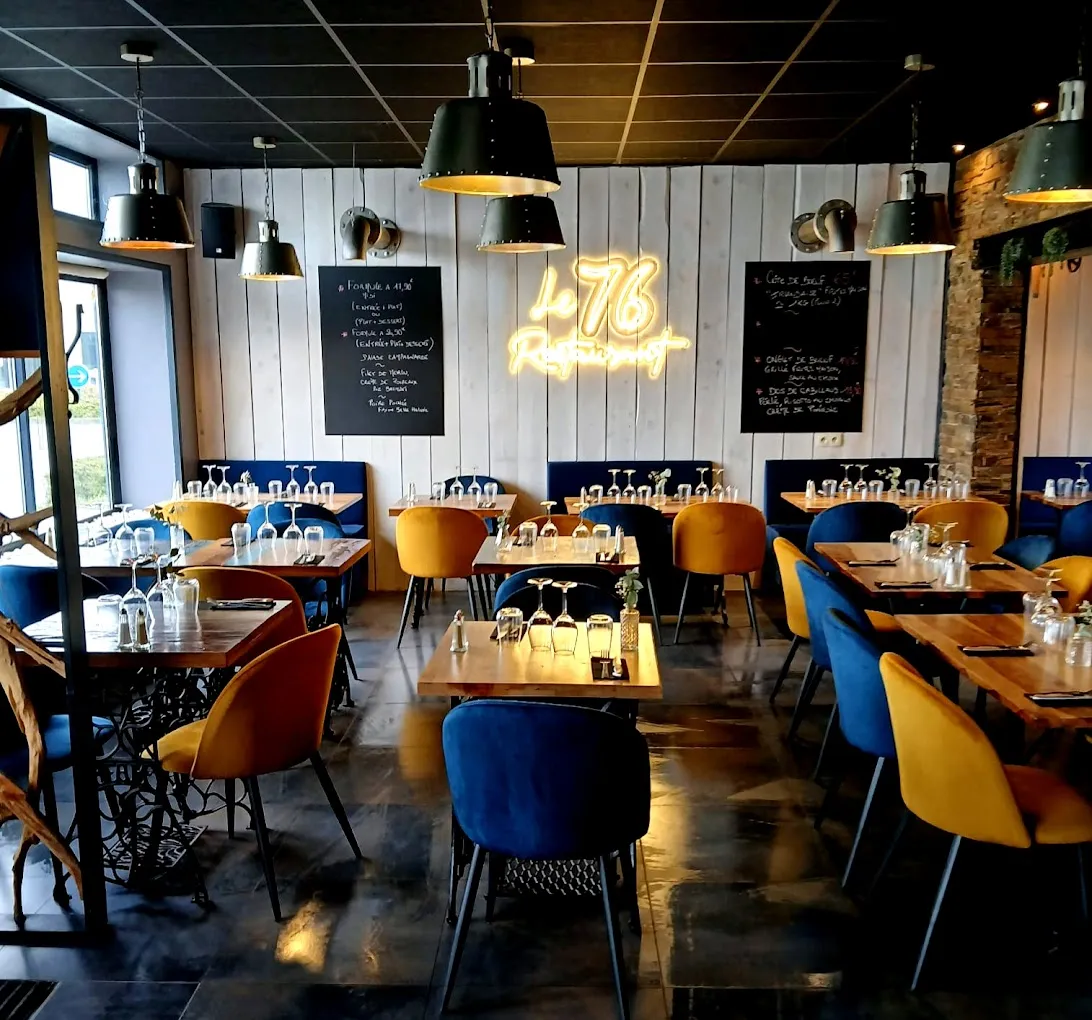 La salle du restaurant, fauteuils bleus et moutarde, enseigne néon « Le 76 ».