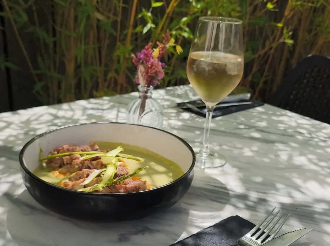 Une table dressée en terrasse : un plat et un verre de vin blanc, à l’ombre des bambous.